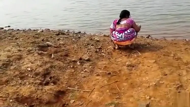 Indian woman peeing in the dirt by a lake